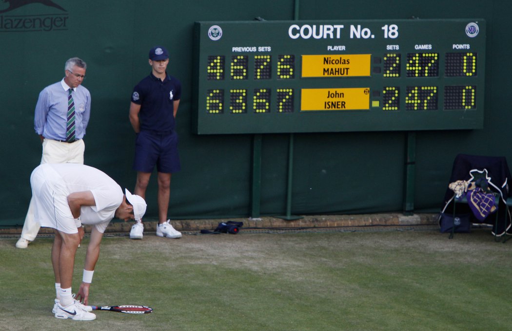 Isner sbírá unaveně z dvorce raketu.