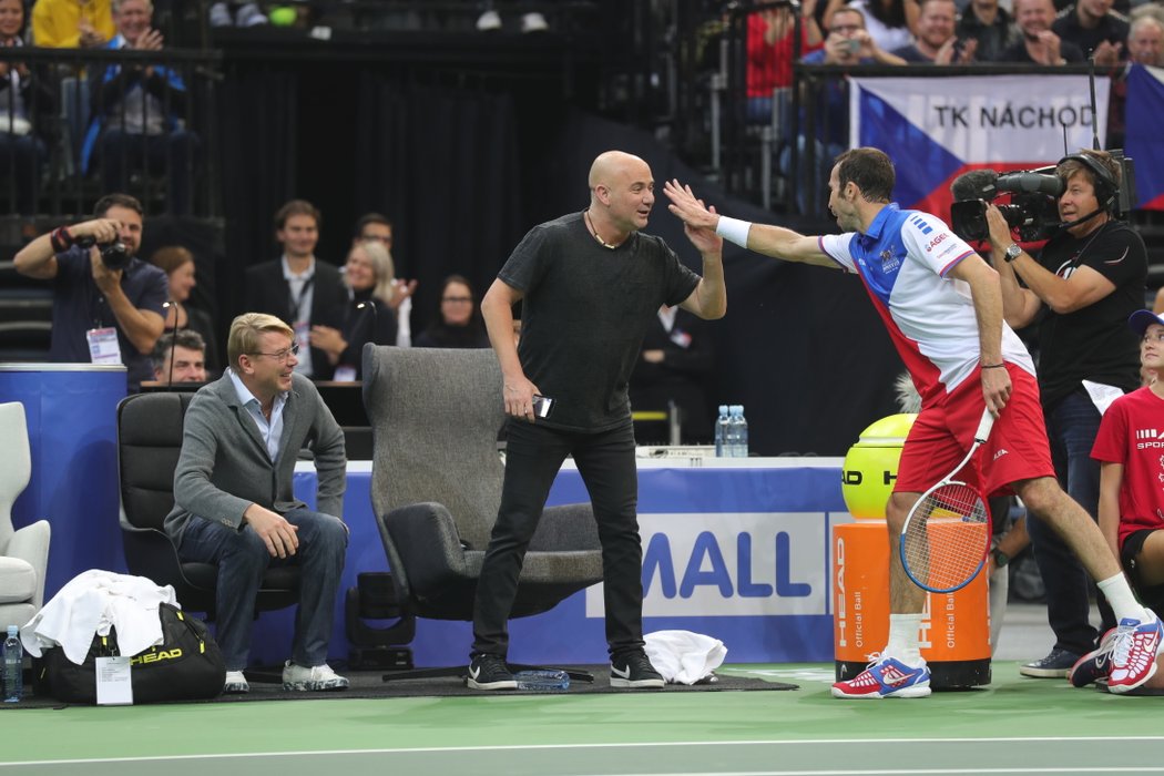 Radek Štěpánek si plácá se &#34;soupeřem&#34; Andrém Agassim, vlevo vše sleduje Mika Häkkinen