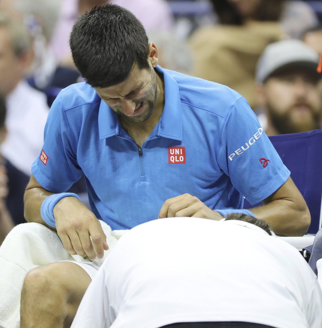 Novak Djokovič křiví obličej bolestí při lékařském ošetření ve finále US Open