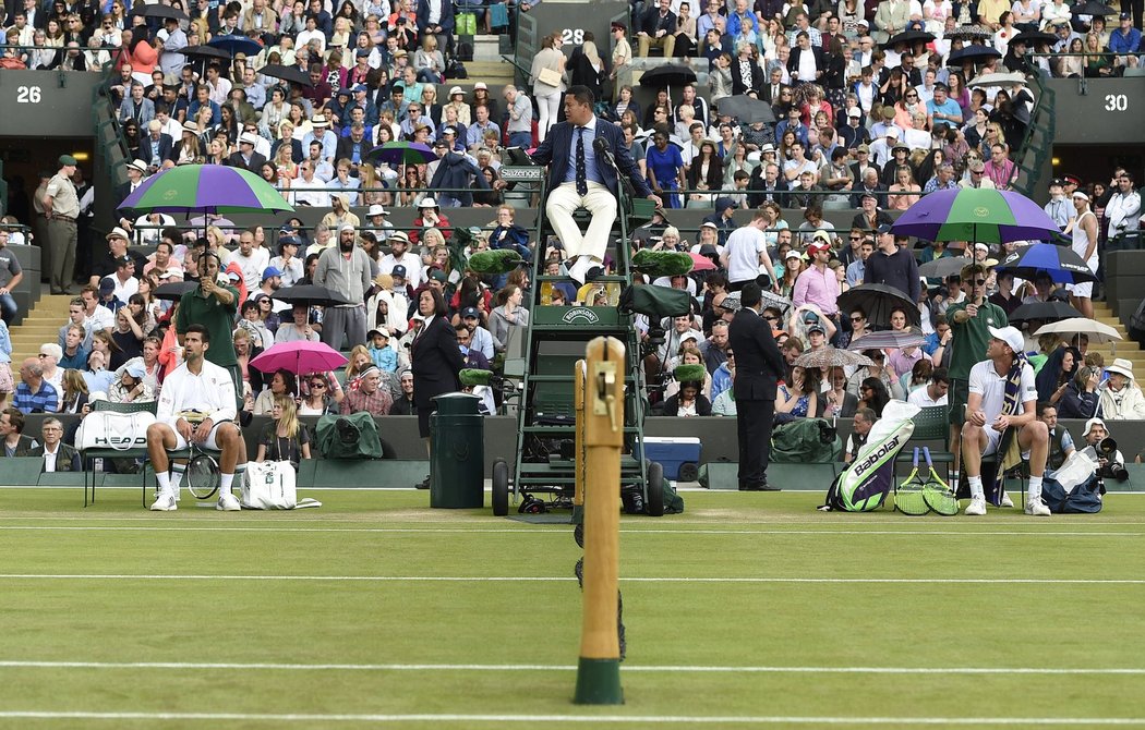 Novak Djokovič (vlevo) a Sam Querrey pod deštníky sledují další přeháňku, která přerušila Wimbledon