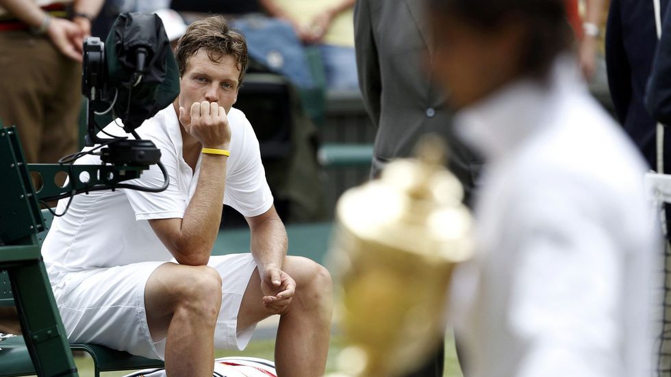 Tomáš Berdych smutně kouká po Rafaelu Nadalovi, který si odnásší pohár po wimbledonského šampiona.