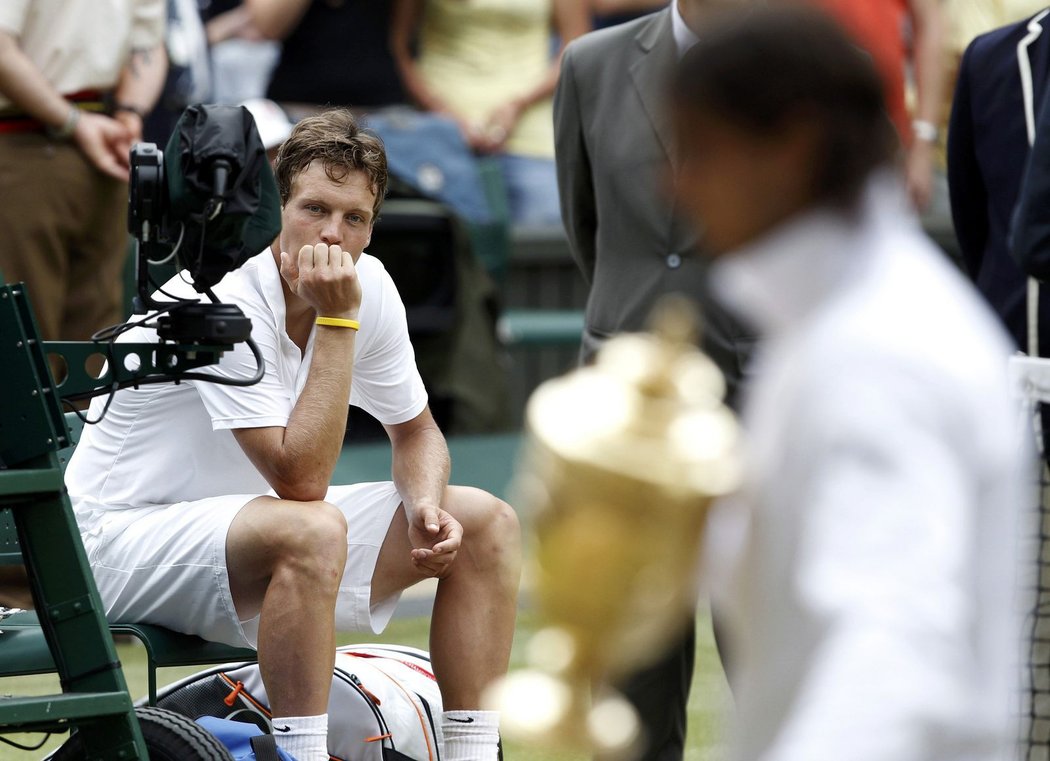 Tomáš Berdych smutně kouká po Rafaelu Nadalovi, který si odnásší pohár po wimbledonského šampiona.