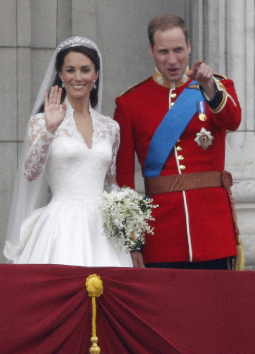 Princ William ukazuje na někoho z balkónu