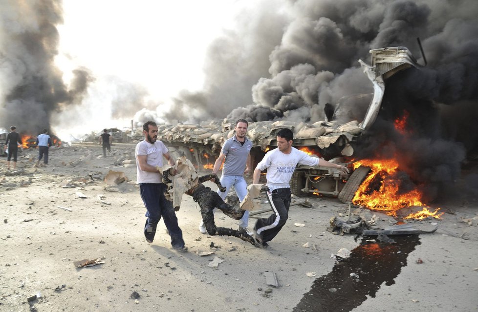 Syřané odnášejí z místa útoku jedno z ohořelých těl. Podobných jsou na místě desítky.
