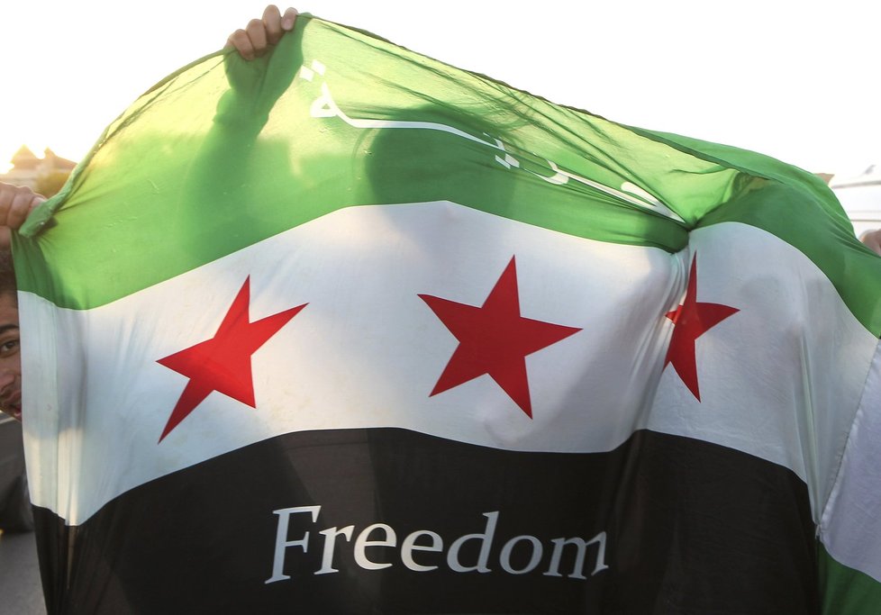 Syrský uprchlík se schovává za vlajkou syrské opoziční armády na demonstraci proti prezidentu Assadovi: V Sýrii i přes přímluvy OSN boje pokračují