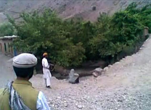 Talibánský ozbrojenec přistupuje zezadu k ženě sedící na ulici