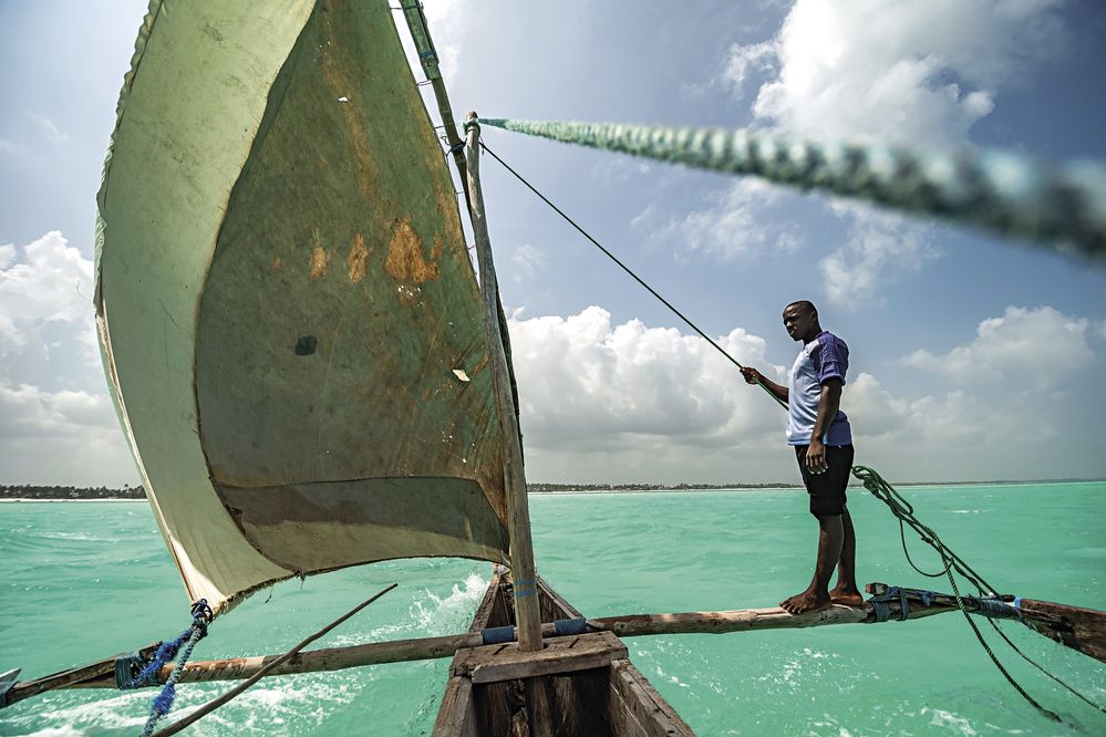 Plachtění na tradičním katamaránu v tyrkysových vodách Zanzibaru. V zimním období foukají silné větry a dřevěný člun sviští po mořské hladině až nebezpečně rychle.