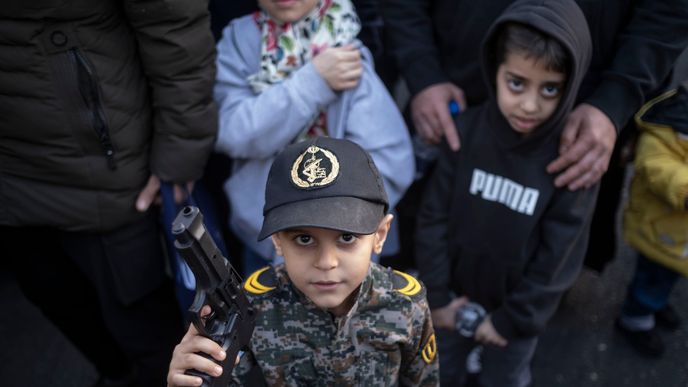 Mladý íránský chlapec v vojenské uniformě pózuje s plastovou zbraní pro fotografy během provládní demonstrace v centru Teheránu. Mladý íránský chlapec v vojenské uniformě pózuje s plastovou zbraní pro fotografy během provládní demonstrace v centru Teheránu.