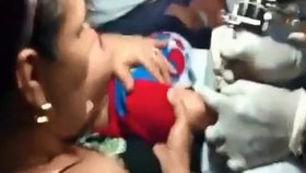 Na šokujícím videu je vidět, jak matka svírá svoje dítě v náručí a nechává mu dělat tetování.