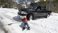 Řidič v Austinu zaskočený mrazy se na svou dodávku pokouší namontovat sněžné řetězy.
