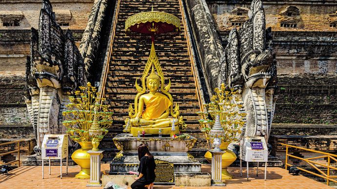 Věřící žena zapaluje vonnou tyčinku během modlitby v komplexu chrámu Wat Chedi Luang v Chiang Mai