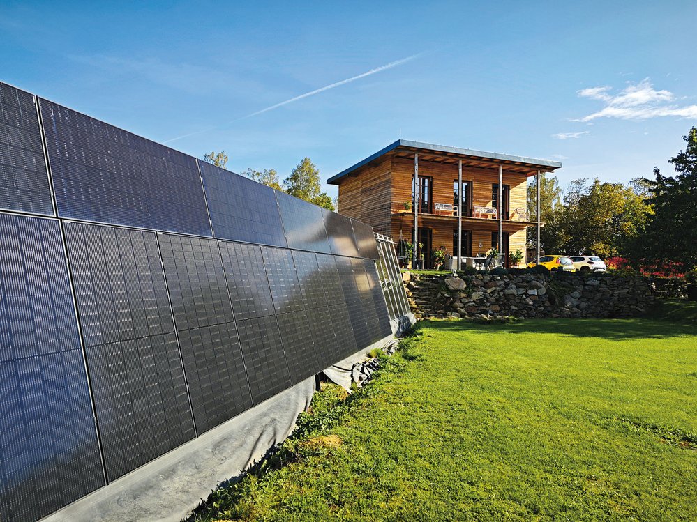 Dřevěný dům se slaměnou izolací Radkových rodičů a v popředí skleník se solárními kolektory. Vlevo je vidět Radkův domeček