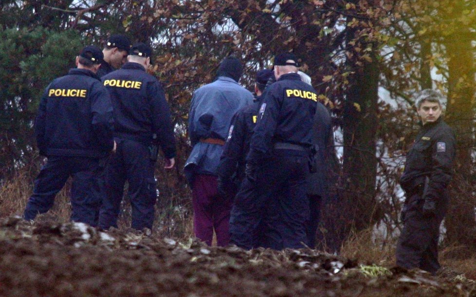 Tomáš Beran ( v černé kukle) při rekonstrukci přímo na místě činu. Policistům líčil a ukazoval, jak dívku zavraždil, rozřezal a jejího těla se zbavil.