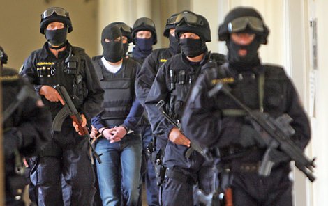 Ozbrojená justiční stráž přivádí kuklou zahaleného Pitra (uprostřed).