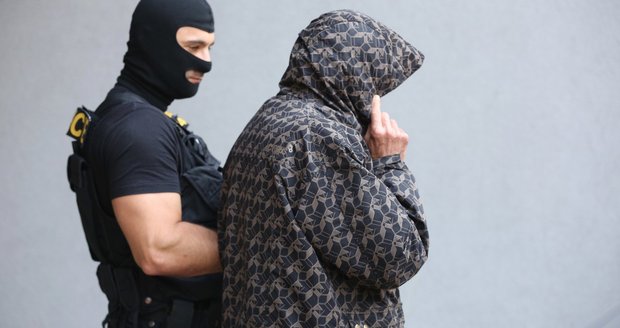 Policista odvádí vraha od soudu, který rozhodl o uvalení vazby.