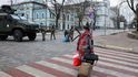Žena kráčí v blízkosti příslušníků ukrajinské vojenské služby střežící silnici v Kyjevě
