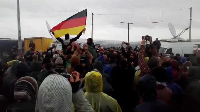 Uprchlíci v táboře Idomeni skandují s německou vlajkou.