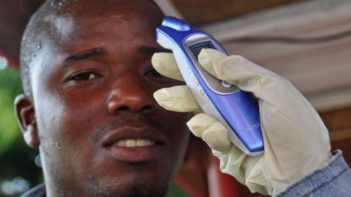 Úřednik měří teplotu muži předtím, než je vpustí do obchodního centra v liberijské metropoli Monrovia