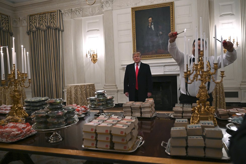 USA v době rozpočtové krize. Prezident Trump musel za vlastní peníze uspořádat hostinu pro univerzitní sportovce, objednal jim pizzu a hamburgery z &#34;Mekáče&#34;.