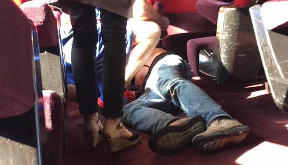 Zraněný muž leží na zemi ve vlaku.