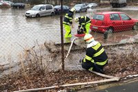 Voda z prasklého potrubí zaplavila parkoviště v Dolních Měcholupech: Hasiči lagunu odčerpávají