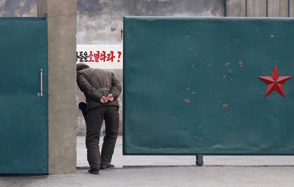 Severokorejský hlídač nahlíží za vrata vojenského areálu