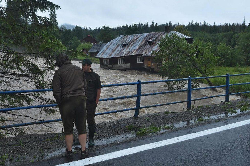 Dva muži pozorují rozvodněný potok Javorinka, který odnáší starý dům v Podspádoch ve Vysokých Tatrách.