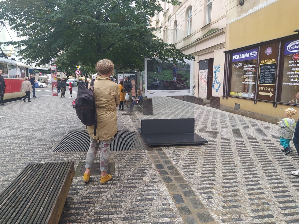 Fotografie si se zájmem prohlížejí kolemjdoucí Pražané i ti, kteří čekají na příjezd tramvaje.