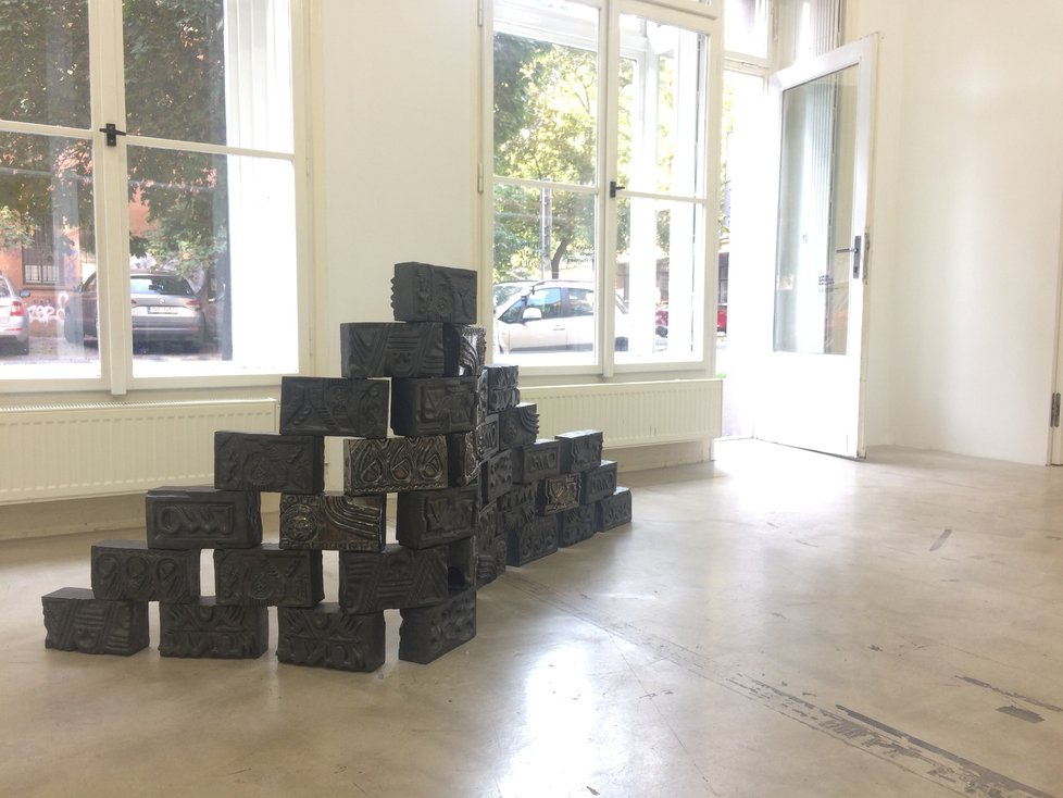 Černé kostky s různými motivy v kompozici, která se jmenuje Another Brick in the Wall dodala na výstavu Sharon Van Overmeiren.