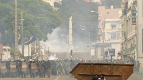 Policejní zásah při pouličních nepokojích v Argentině. Muži se schovávají za kontejnerem