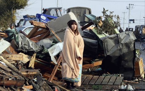 Symbol katastrofy Yuko Sugimoto stojí zabalená v dece mezi troskami.