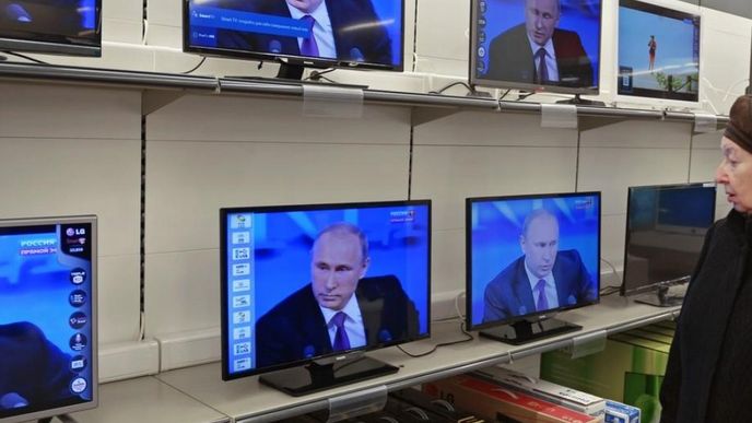 Zákaznice prodejny s elektronikou v Moskvě sleduje tradiční výroční konferenci ruského prezidenta Vladimira Putina