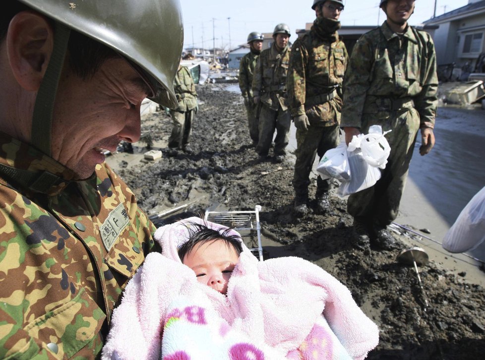 Člen japonských ozbrojených sil s úsměvem na tváři a zachráněnou čtyřměsíční holčičku v náručí v Ishimaki na severu Japonska.