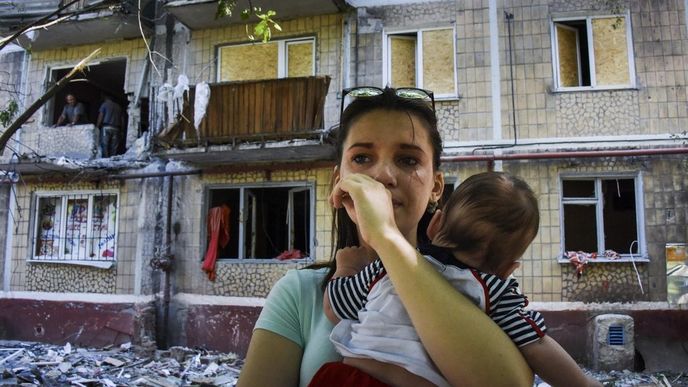 Žena před poškoženým domem na východě Ukrajiny
